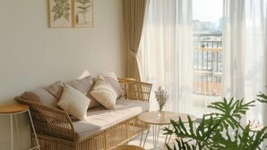 Ein gemütliches Zimmer mit einem Rattan-Sofa, einem kleinen runden Tisch und Blick auf die Stadt durch transparente Vorhänge.