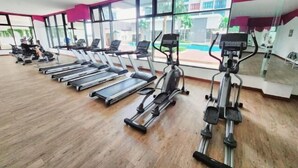 A gym with treadmills, elliptical machines, and a large window offering a view of a swimming pool and buildings. - Conezion at Putrajaya #IOI CITY MALL #7 Pax #NEW (Serdang)