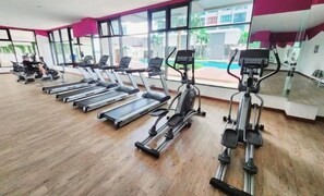A gym with treadmills, elliptical machines, and a large window offering a view of a swimming pool and buildings. - Conezion at Putrajaya #IOI CITY MALL #7 Pax #NEW (Serdang)