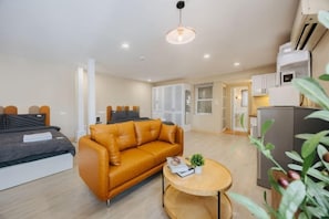 A modern living room with a sofa, a coffee table, and a bed. There is a kitchenette area with cabinets and a refrigerator. - VietHOME - 22 Pho Hue - Apartment 502 (Hanoi)