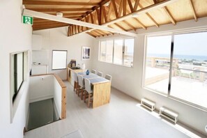 A modern interior with a wooden ceiling, a dining area with a long table and chairs, large windows with a view, and a small kitchenette. - and SEA The Terrace (Kamogawa)