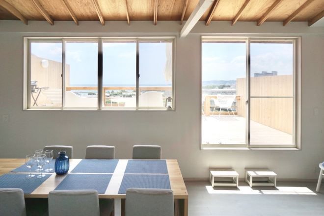Una habitación con una mesa grande, sillas y dos ventanas que dan a vistas del exterior.