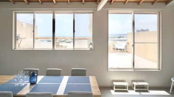 Una habitación con una mesa grande, sillas y dos ventanas que dan a vistas del exterior.