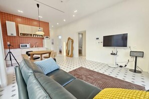 Una sala moderna con sofá, mesa de comedor, televisor y área de cocina con microondas.