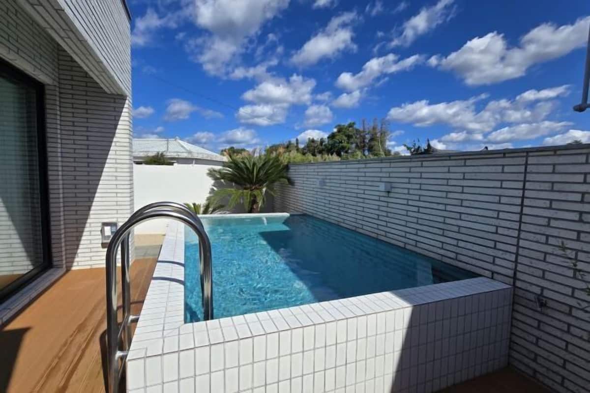 A swimming pool with a tiled deck, surrounded by a white brick wall, under a clear sky.
