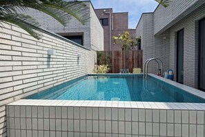 Una piscina con bordes de azulejos, una valla de madera y un edificio moderno con fachada de ladrillo al fondo.