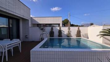 Una piscina moderna al aire libre con bordes de azulejos, una cerca blanca y un cielo despejado.