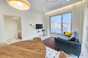 Un moderno salón con una mesa de comedor de madera, un sofá con cojines, un televisor de pantalla plana y un ventanal con vistas a un paisaje nevado.