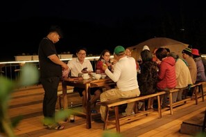 A group of people dining outdoors at night on a wooden deck with a railing. - Mountain Nest Villa Dalat - BBQ, Cloud Hunting, Camping (Lac Duong District)