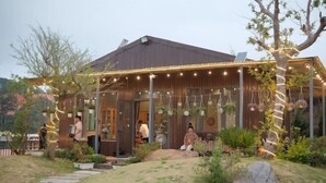 A rustic wooden house with a covered porch, stone pathway, and hanging lights. - Mountain Nest Villa Dalat - BBQ, Cloud Hunting, Camping (Lac Duong District)