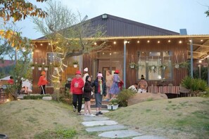 A building with a covered outdoor area, a pathway leading to the entrance, and a group of people gathered outside. - Mountain Nest Villa Dalat - BBQ, Cloud Hunting, Camping (Lac Duong District)