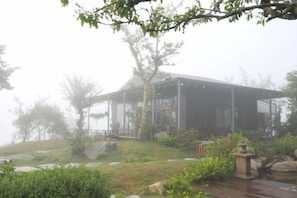 A building with a covered outdoor area, surrounded by greenery and a body of water. - Mountain Nest Villa Dalat - BBQ, Cloud Hunting, Camping (Lac Duong District)