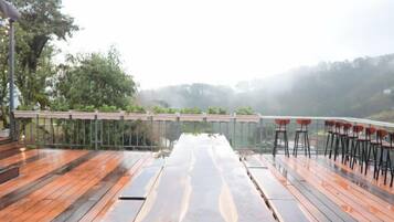 A wooden deck with a long table and chairs, overlooking a misty landscape.