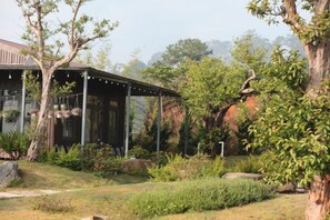 A covered outdoor area with a wooden structure, surrounded by greenery and rocks. - Mountain Nest Villa Dalat - BBQ, Cloud Hunting, Camping (Lac Duong District)