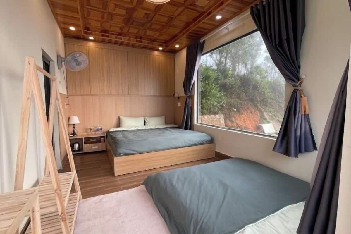 A bedroom with a wooden ceiling, a large window with curtains, a bed, a bedside table, and a nightstand.