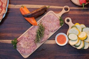 A wooden cutting board with sliced meat, vegetables, and a small bowl of sauce. - Mountain Nest Villa Dalat - BBQ, Cloud Hunting, Camping (Lac Duong District)