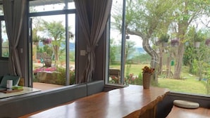 A room with a large window, a wooden bench, and a view of a garden. - Mountain Nest Villa Dalat - BBQ, Cloud Hunting, Camping (Lac Duong District)