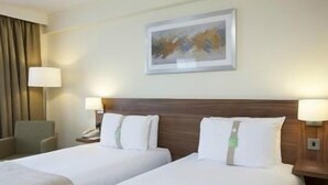 Habitación de hotel con dos camas, cabecero de madera, un cuadro en la pared y dos lámparas de noche.