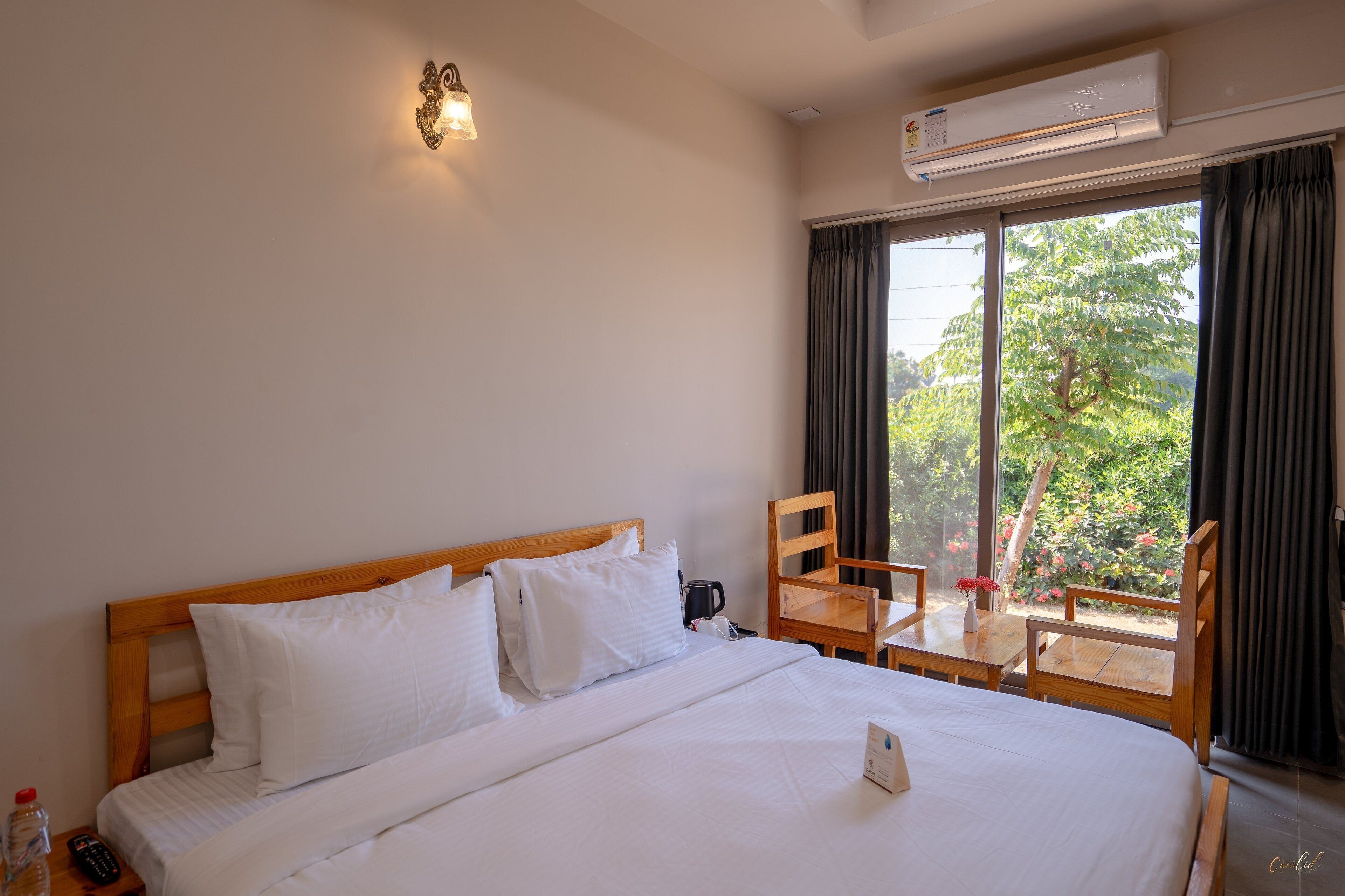 A hotel room with a large bed, a wooden headboard, a bedside table with a remote control, a coffee maker, and a small table with a vase of flowers.