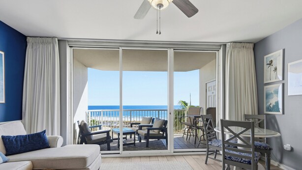 A room with a sofa, a dining table, chairs, and a view of the beach.