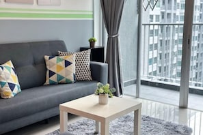 A modern living room with a grey sofa, patterned cushions, a small table with a plant, and a view of a cityscape through large windows. - Razak City Residences A3 by Favspace (Kuala Lumpur)