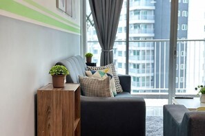 Een moderne woonkamer met een bank, een houten bijzettafeltje en een uitzicht op een stadsgezicht door grote ramen.