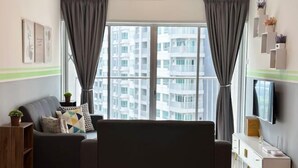 A modern living room with a grey sofa, a TV on the wall, and a large window with curtains. - Razak City Residences A3 by Favspace (Kuala Lumpur)
