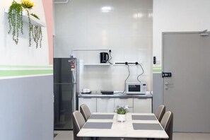 A small kitchenette with a microwave, refrigerator, and a coffee maker. There is a table with chairs and a potted plant. - Razak City Residences A3 by Favspace (Kuala Lumpur)