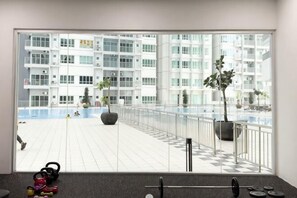Een sportschool met fitnessapparatuur, een groot raam met uitzicht op een gebouw en een zwembad.