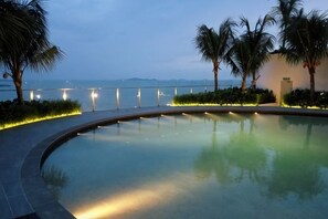 A curved pool with a view of the sea and mountains, surrounded by palm trees and illuminated pathways. - Bella Vista Silverscape Seaview Homestay (Melaka)