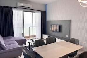Ett hotellrum med en soffa, ett matbord, stolar, en TV och en balkong med gardiner.