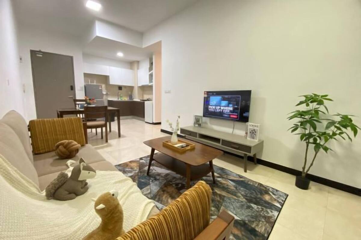 A modern living room with a sofa, a coffee table, and a television. There is a kitchen area in the background.