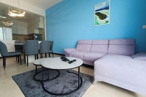 A living room with a purple sofa, a round coffee table, and a dining area with chairs and a table.