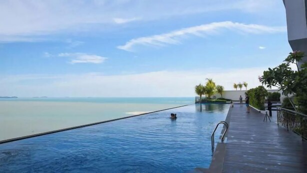 A infinity pool with a view of the sea, a wooden deck, and palm trees. - Bella Vista Silverscape Seaview Homestay (Melaka)