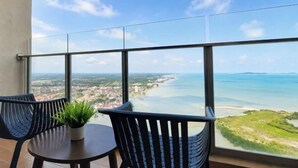 A balcony with a view of a beach and cityscape, two chairs, and a small table with a plant. - Bella Vista Silverscape Seaview Homestay (Melaka)