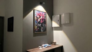 A hallway with a framed floral artwork, a wooden bench, and a wall-mounted light fixture. - Entire Unit & 2BR Near Legoland (Iskandar Puteri)