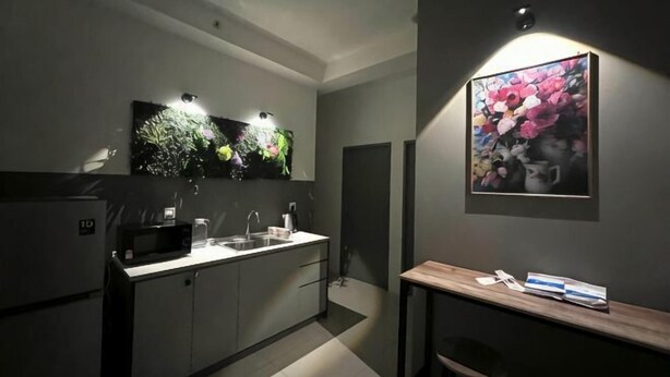A modern kitchen with a microwave, sink, and cabinets, a wooden table with a chair, and a wall-mounted artwork. - Entire Unit & 2BR Near Legoland (Iskandar Puteri)
