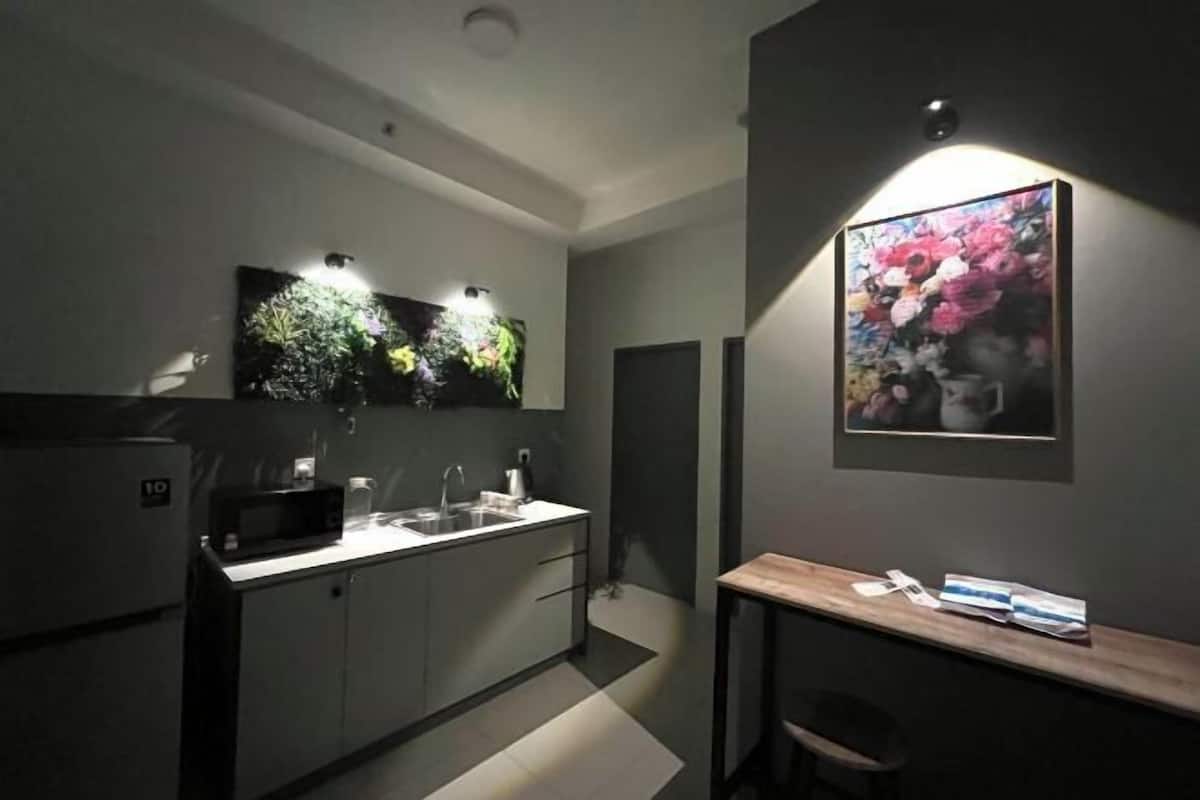 A modern kitchen with a microwave, sink, and cabinets, a small table with a chair, and a framed floral artwork on the wall.
