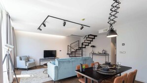 A modern living room with a TV, sofa, dining table, and staircase.