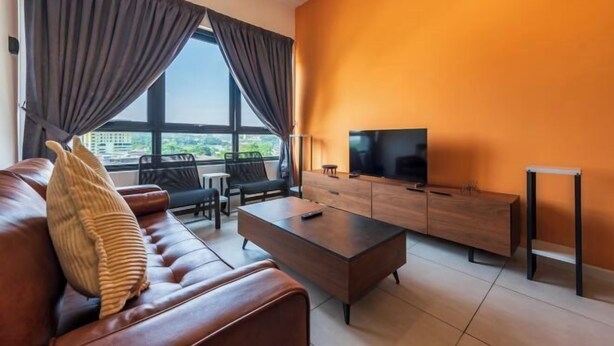 A modern living room with a sofa, coffee table, and TV, featuring a large window and orange walls. - The Pano by Minsu (Kuala Lumpur)