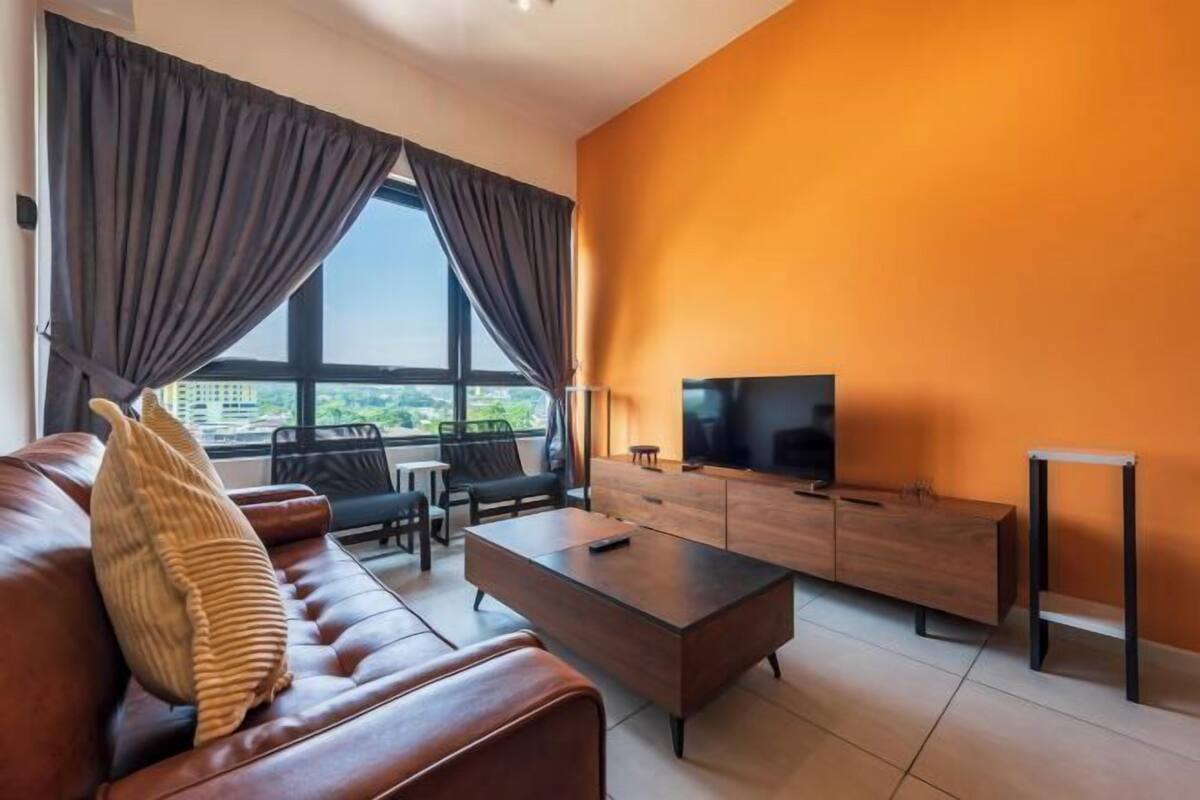 A modern living room with a sofa, coffee table, and TV, featuring a large window and orange walls.