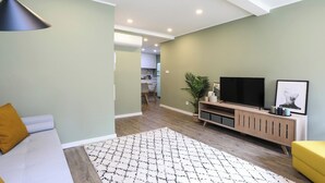 Een moderne woonkamer met een bank, een televisie op een houten dressoir en een vloerkleed met dessin.