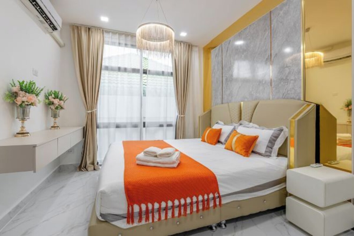Una habitación de hotel moderna con una cama grande, una mesita de noche y un ventanal con cortinas.