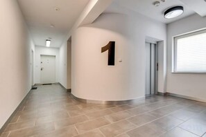 A hallway with a number 1 sign, a door, and a window with blinds. - GreenApartments (Chorzow)