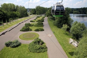 Eine Seilbahn, ein gepflasterter Weg und eine Grünanlage mit Bäumen und einem See.