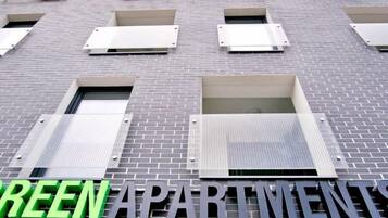 A building with a sign reading 'GREEN APARTMENT' and multiple windows with blinds.