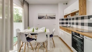 A modern kitchen with white cabinets, a black and white checkered backsplash, and a dining area with a white table and chairs. - GreenApartments (Chorzow)