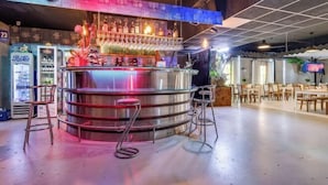 A bar area with a stainless steel counter, bar stools, and a variety of bottles and glasses. - GreenApartments (Chorzow)