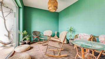 A room with a wooden floor, wicker furniture, a glass table, and a hanging light fixture.