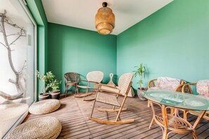 A room with a wooden floor, wicker furniture, a glass table, and a hanging light fixture. - GreenApartments (Chorzow)